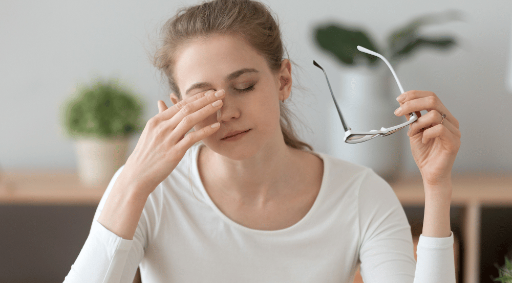 woman taking off her glasses and holding a hand to her face due to discomfort