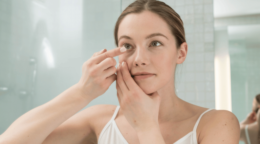 younger woman inserting contact lens in the bathroom